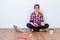 Dreamy student hipster is sitting on the floor at home with crossed legs, studying with books, laptop and cup of coffee. He is in