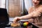 Dreamy woman holding bowl with musli breakfast and fresh fruits while sitting near laptop