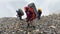 Drenched tourists with large backpacks walk on slippery stones in heavy rain.