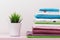 On the dresser there is a stack of clean ironed bed linen, folded multi-colored towels and a home plant stands