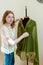 Dressmaker with measuring tape draping green cloth on mannequin and looking at camera