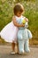 Dressy two-year-old girl in pink dress holding stuffed bear and flower