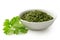 Dried chopped coriander leaves in white ceramic bowl next to fresh coriander leaves isolated on white