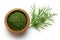 Dried chopped dill in a dark wood bowl next to fresh dill leaves isolated on white from above