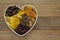 Dried fruits mix, in wooden heart shape box isolated on wooden background. Top view of various dried fruits figs, apricots, mango