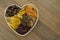 Dried fruits mix, in wooden heart shape box isolated on wooden background. Top view of various dried fruits figs, apricots, mango