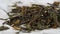 Dried green leaves of herbal hemp tea fall onto a white paper napkin