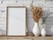 Dried plants in a vase next to a wooden frame mockup on a wooden table against a white brick wall