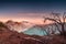 Dried tree on active volcano crater with turquoise lake at dawn