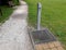 Drinking fountain in a city park for visitors walking on a footpath lawn gravel path gray metal drinking fountain prism post with