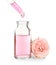 Dripping rose essential oil from pipette into bottle and flower on white
