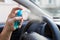 Driver hand holding bottle spray of sanitizer to protect car steering wheel from bacteria. Antiseptic, hygiene and healthcare