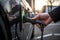 A driver\\\'s hand plugging in an electric car charger at a public charging station, on a background of sunset.