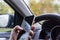 Driver`s hand with smartphone on steering wheel of car