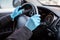 Drivers hands in blue rubber gloves holding steering wheel of car, close-up view