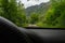 Driving car in the mountain in a path with green forest and big rocks. Driver view with black steering wheel