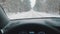 Driving the car during the winter on the snow covered road surrounded by tall leafless trees. Point of view shot