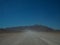 Driving through dusty unpaved road to rocky mountain among desert landscape