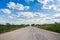 Driving on an empty road. Empty asphalt road through the green field and clouds on blue sky in summer day. Open road ahead, endles