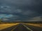 Driving offroad car through black raining cloud on highway road trip through savannah dried grass landscape