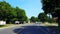 Driving residential city road with lush trees during summer day. Driver point of view pov along beautiful sunny street.