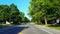 Driving residential city road with lush trees during summer day. Driver point of view pov along beautiful sunny street.