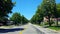 Driving Residential City Road With Lush Trees During Summer Day.  Driver Point of View POV Along Beautiful Sunny Suburban Road