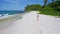 Drone aerial follows young woman walking on the paradise Anse Bazarca beach. Aerial 4k footage view of tanned girl on