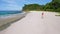 Drone aerial follows young woman walking on the paradise Anse Bazarca beach. Aerial 4k footage view of tanned girl on