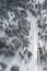 Drone aerial of a frozen dangerous road crossing a snowy forest mountain in winter.