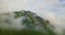 Drone aerial view flying above the clouds towards a beautiful green mountain scenary