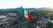 Drone-Aerial view of a huge mexican flag waving, at back the sun is hiding behind the mountains. Many cars transit for the avenue.