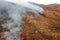 Drone aerial view of wildfire in the mountains. Overhead view on burning trees and grass among the rocky mountains. Seasonal fires