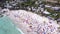 Drone of beach, ocean and people swimming by holiday houses and relax on sand for travel, hospitality or vacation