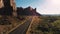Drone camera follows car driving along small desert highway road near breathtaking steep canyon ridge on sunset in USA.