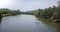 Drone camera follows and flies past little white boat sailing in the middle of beautiful calm river in rainforest jungle