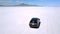 Drone camera follows silver minivan car driving towards far mountains on breathtaking landscape of flat salt lake desert