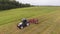 Drone camera view of big grey tractor moving with working red round shaped rakes