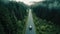 A drone captures a car driving along a highway nestled within a forest