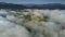 Drone flies above white clouds swirling at hill peaks