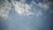 The drone flies against a background of blue sky and clouds, a view from below. The quadcopter with the camera hovers at