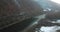 A drone flies along over a winter river on the snow shore.