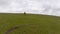 The drone flies behind an athletic man pedaling an MTB bike up a steep grassy hill. Beautiful view of the mountains in