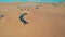 A drone flies over a caravan of buggies standing on a desert sand dune.