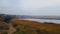 Drone flies under low rain clouds moving over dry yellow reeds and pacific blue river. Deep autumn aerial shot