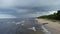 Drone flight along the beach and sea with rain clouds. Coastline perspective with rolling waves