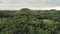 Drone fly over rainforest to Chocolate Hills with lush greenery. White cottages under trees leaves