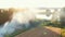 Drone flying above camping spot with fire, cars and tents towards large lake and epic summer sunrise lens flare panorama