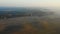 Drone flying above epic autumn field and forest covered with sunset mist towards foggy skyline. Peaceful pastoral nature