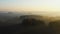 Drone flying above vast atmospheric field, autumn forest covered with mist towards foggy sunset skyline panorama.